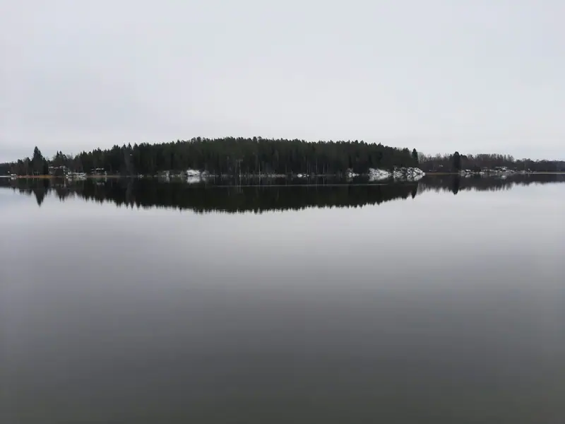 Tyyni Keijärvi Ylöjärvellä joulukuussa. Metsäinen niemi heijastuu veteen, ja rannoilla on ensilunta.