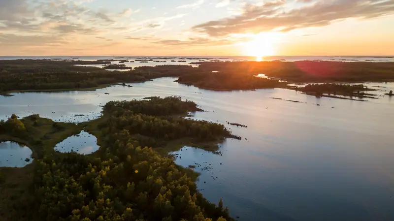 Ilmakuva Merenkurkun saaristosta auringonlaskun aikaan, metsäisiä saaria ja tyyntä vettä.