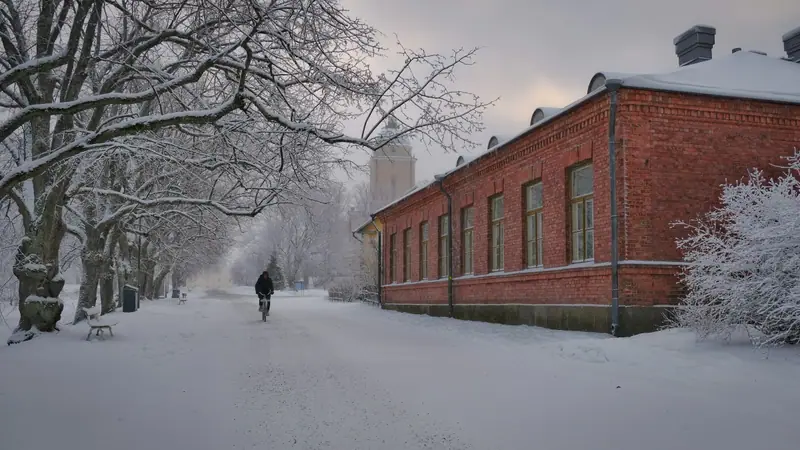 Luminen tie punatiilisen rakennuksen vieressä Suomenlinnassa, kauempana pyöräilijä huurteisten puiden alla.